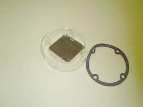 Luftklappe von Remeha bestehend aus einem rechteckigen Metallteil in einer transparenten Halterung, begleitet von einem Gummiring zur Abdichtung.